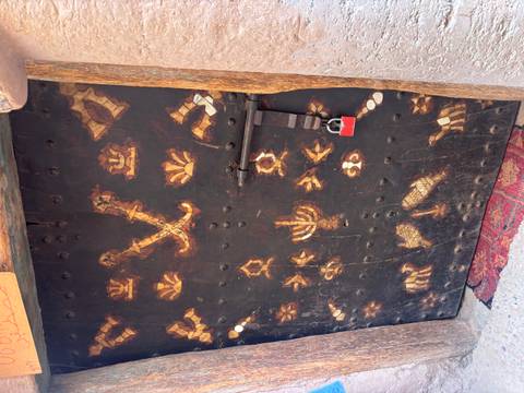 Old wooden door with intricate inlay patterns and a red padlock in a Moroccan alley.