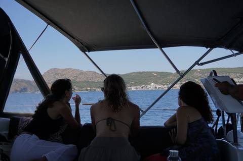 Three travellers relaxing under the shaded cockpit of a sailboat looking out to coastal hills.