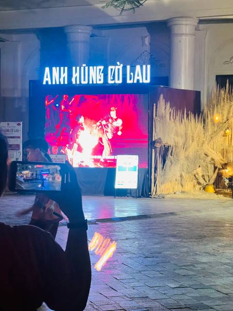 Blurry night street performance displayed on a large screen with phone recording in foreground