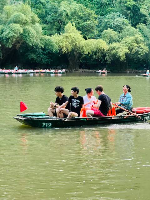 Tourists ride in a small rowboat on green river with life vests and flag