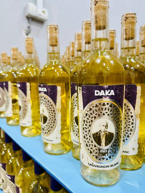 Rows of golden bottles labeled "DAKA" are neatly lined up on a shelf, showcasing a local beverage.