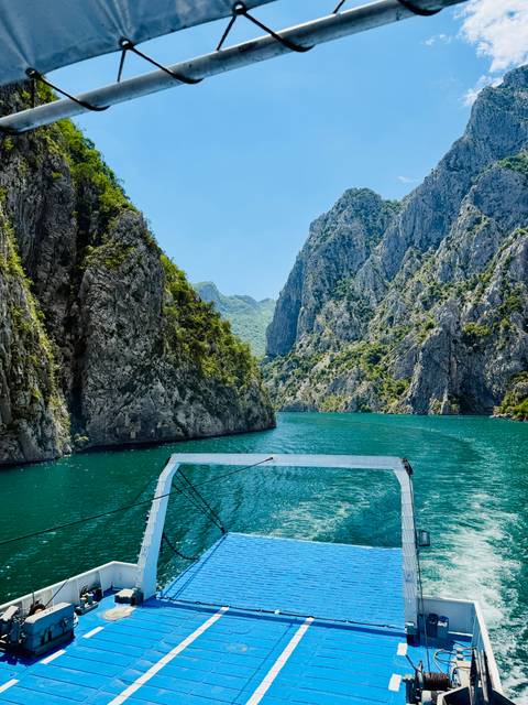Turquoise water winds through steep rocky cliffs in a dramatic canyon, viewed from the bow of a small boat.
