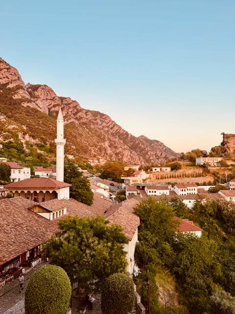 Mountain town at golden hour with slim white minaret rising above tiled rooftops and rugged cliffs