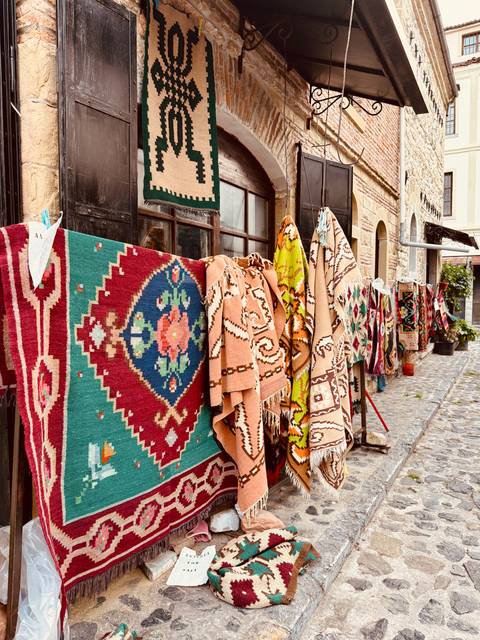 Row of brightly patterned carpets and kilims hanging outside a stone lane shop