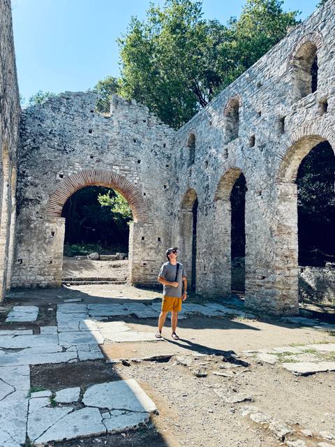 Explorer standing among towering stone arches of a historic ruined basilica surrounded by forest