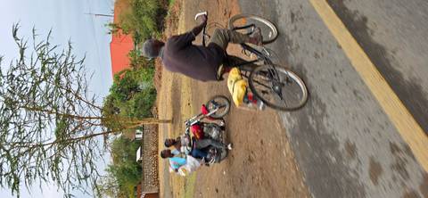 Local men ride a bicycle and motorbike along a rural Kenyan road.
