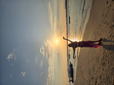 Silhouette of a woman on a sandy beach at sunset with boats on the water.