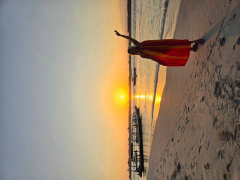 Woman wrapped in a flowing scarf celebrates a golden beach sunrise.