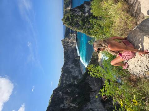 Woman sits on a rock admiring a round turquoise bay framed by high cliffs.