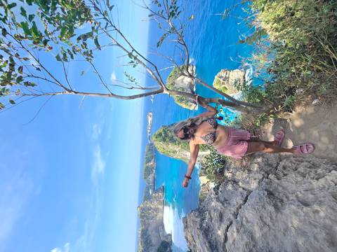 Woman stretches arms on rocky viewpoint above vivid blue sea and islands.
