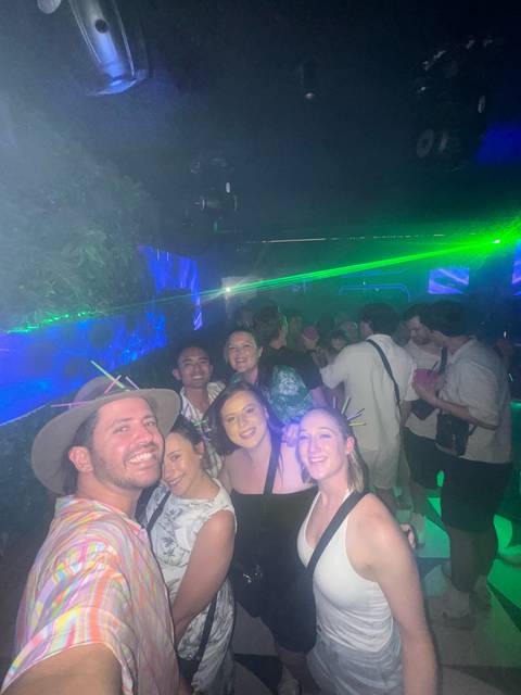 A lively nightclub scene with a group of smiling friends taking a selfie under green laser lights and haze.