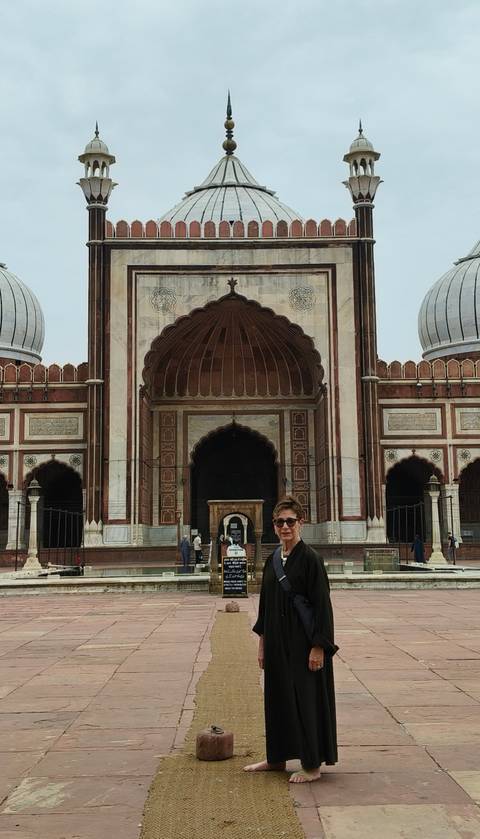 An older traveler poses in front of the grand arched entrance of Jama Masjid mosque.