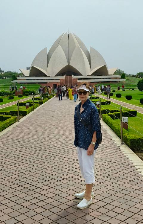A visitor smiles on a brick walkway lined with manicured gardens leading to the Lotus Temple.