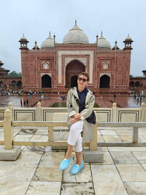 An older traveler poses on a terrace overlooking red-sandstone Mughal architecture after rain.