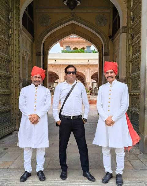 A visitor stands between two traditionally dressed doormen in white uniforms and red turbans.