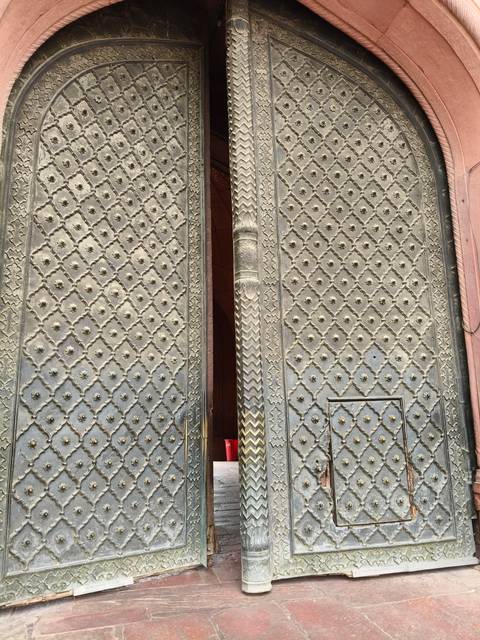 Massive decorative brass doors with embossed floral patterns and studded rivets in an Indian palace.