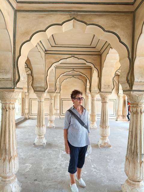 A traveler stands thoughtfully inside a series of elegant cream-colored Mughal arches.