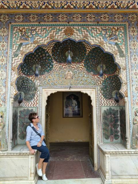 A visitor admires the vibrant Peacock Gate adorned with colorful feathers and floral motifs.