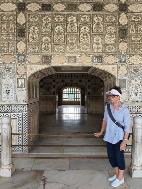 An ornate marble hall with intricate inlay and mirrored walls frames a traveler standing to the side.