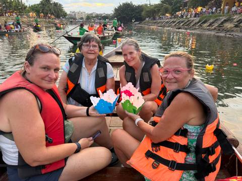 Group of women in life vests float paper lanterns from a wooden skiff on calm water.