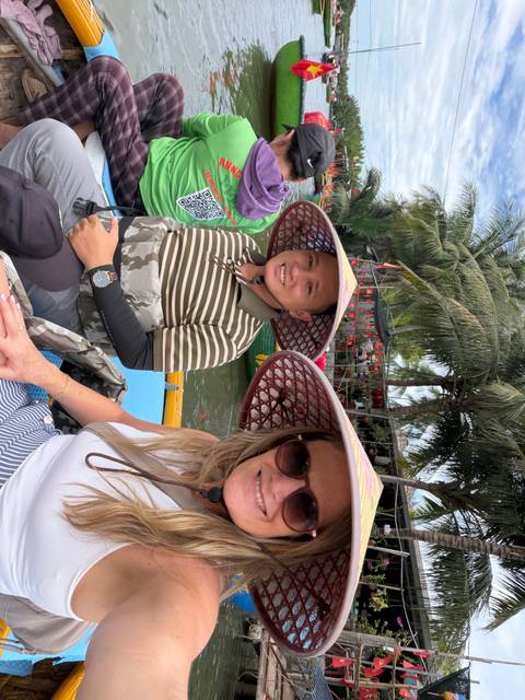 Smiling guide and tourist wearing broad-brim hats in a small river boat under palms.