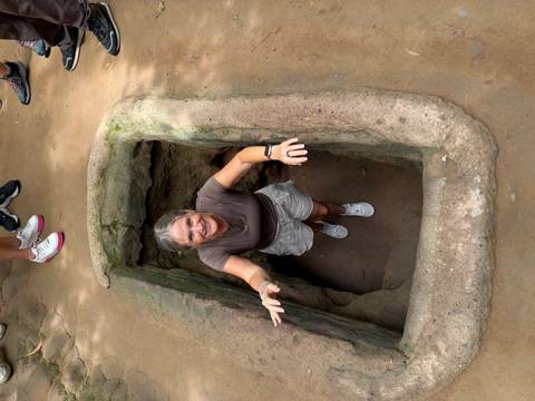 Visitor emerging from a narrow Cu Chi tunnel entrance carved into the ground.