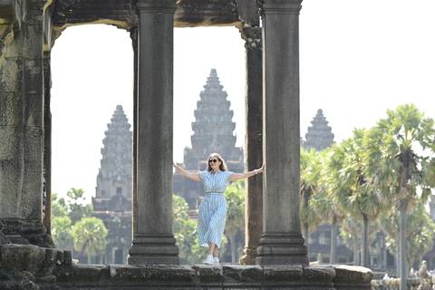 Woman framed by stone columns with the iconic towers of Angkor Wat in the distance.