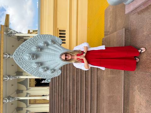 Visitor in red dress stands prayerfully before a multi-headed Naga sculpture at a palace.