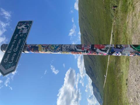 Sticker-covered signpost pointing to Glen Etive stands before expansive Highland scenery.