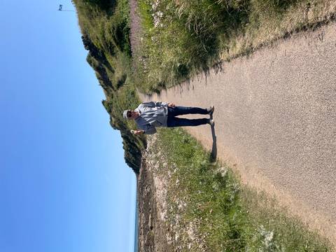 Solo walker on a paved coastal trail bordered by wildflowers and grassy slopes.