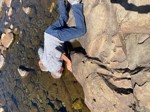 Traveller kneels to drink directly from a clear rocky stream in the Highlands.