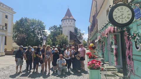 Tour group posing on a cobblestone street lined with pastel buildings and a medieval tower in the background.