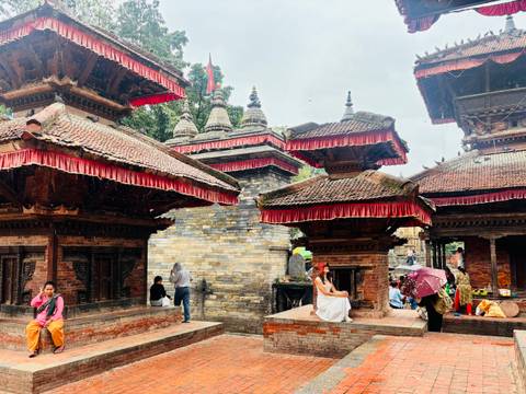 Brick pagoda temples with red roofs in Kathmandu Durbar Square where visitors rest and explore.
