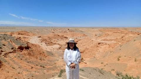 Woman in white stands before the orange sandstone canyons of Mongolia’s Flaming Cliffs under a vast blue sky.