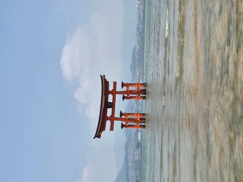 Iconic vermilion Great Torii of Itsukushima Shrine standing in calm seawater with hazy mountains behind.
