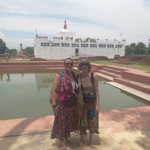 Two women pose beside the sacred pool in front of the white Maya Devi Temple at Lumbini.