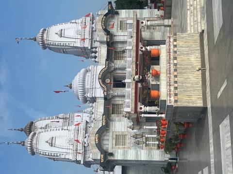 White-marble Hindu temple complex with multiple domed towers against a blue sky.