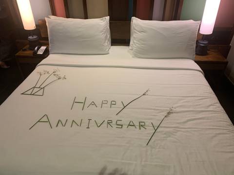 Hotel bed decorated with leaves spelling out 'Happy Anniversary' and small floral accents.