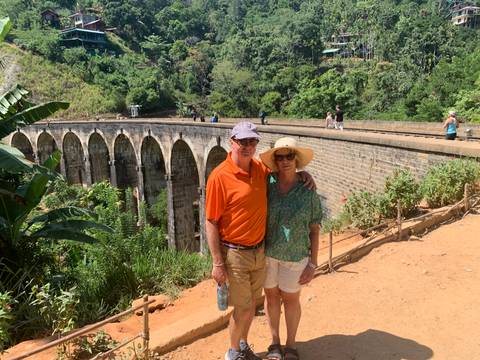 Smiling couple standing on the famous stone Nine-Arch Bridge surrounded by jungle greenery.