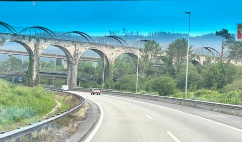 Stone multi-arch viaduct crossing a forested valley viewed from a moving car on the highway.