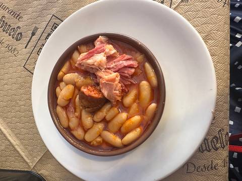 Hearty bowl of white bean stew with ham and chorizo served on a white plate.