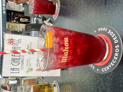 Tall glass of red fruity cocktail on a café table with menu and coasters visible.