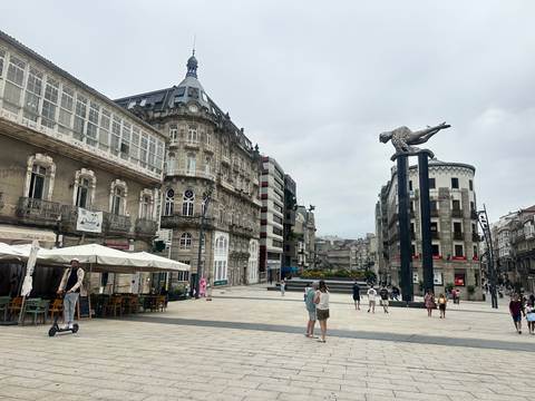 Pedestrian plaza in Vigo featuring historic stone buildings, outdoor cafés, and the modern Sireno sculpture.