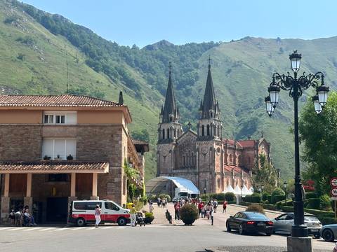 Basilica of Covadonga framed by green mountains with visitors in the foreground on a sunny morning.
