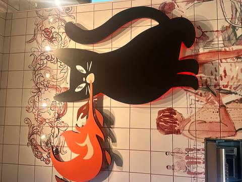 Tile mural of a black cat breathing fire on an interior café wall.