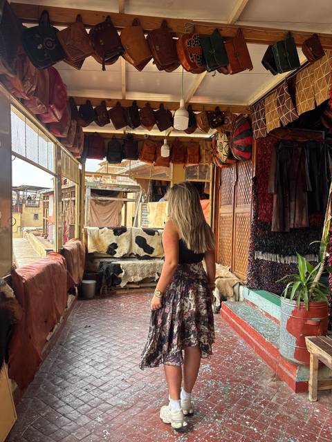 Woman browsing leather goods inside a traditional Moroccan souk lined with rugs and hides.