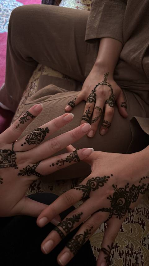 Close-up of fresh henna designs drying on travelers' fingers inside a dim room.