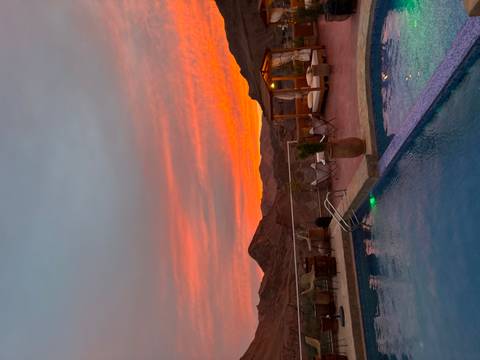 Infinity pool terrace at a desert lodge with vivid orange sunset over rugged hills.