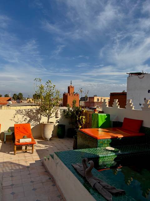 Colorful rooftop terrace in Marrakesh with orange loungers and distant Atlas Mountains.