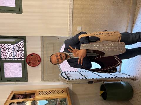 Smiling artisan presenting studded leather bags inside a riad workshop.